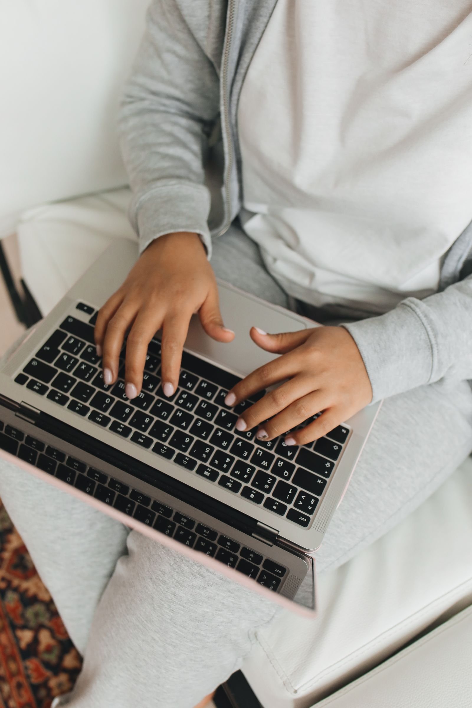Overhead view of a person’s hands typing on a laptop keyboard resting on their lap.